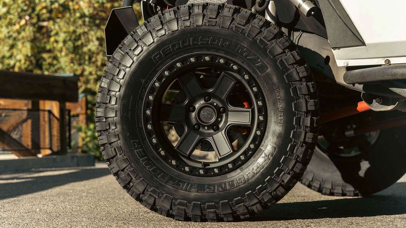 Close-up of an off-road tire with aggressive tread mounted on a black alloy wheel on a white vehicle