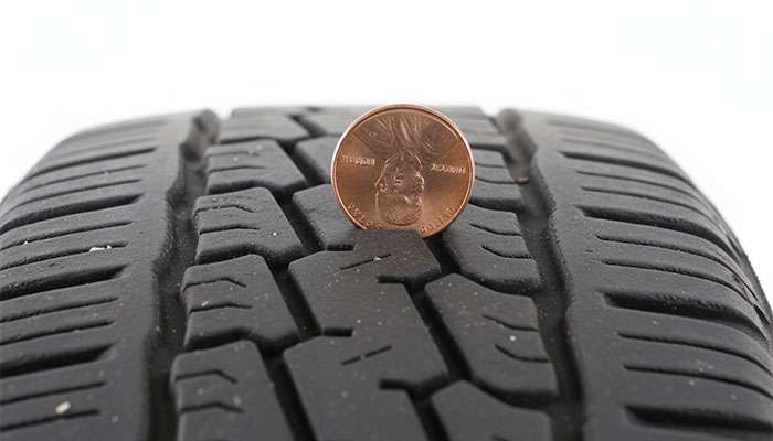 Hand holding a penny upside down to check tire tread depth using the penny test on a worn tire