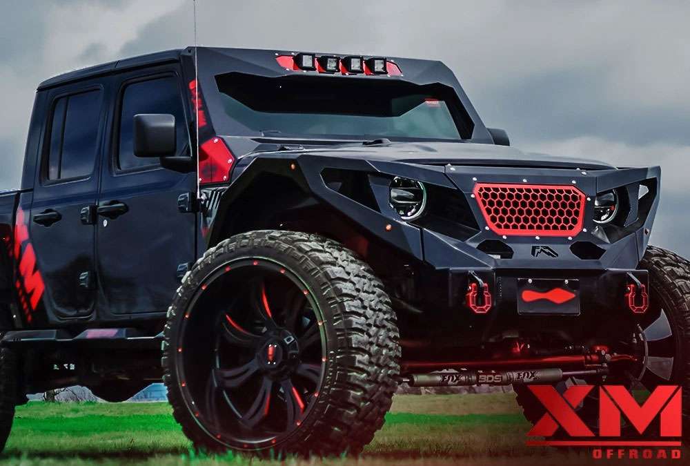 Black and red customized off-road truck with large tires on grassy terrain under a cloudy sky.