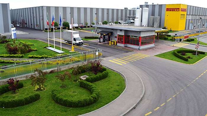 Aerial view of the Pirelli Romania factory entrance with flags, greenery, and a white delivery truck entering the premises
