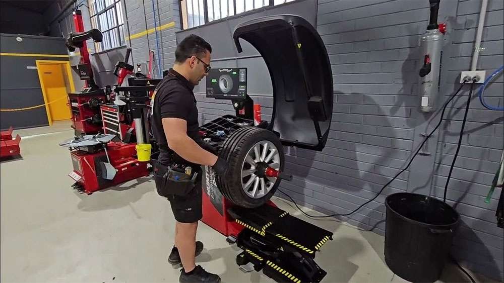 Technician using Hunter Smart Weight Pro SWP90E machine to balance a car tire in a workshop.