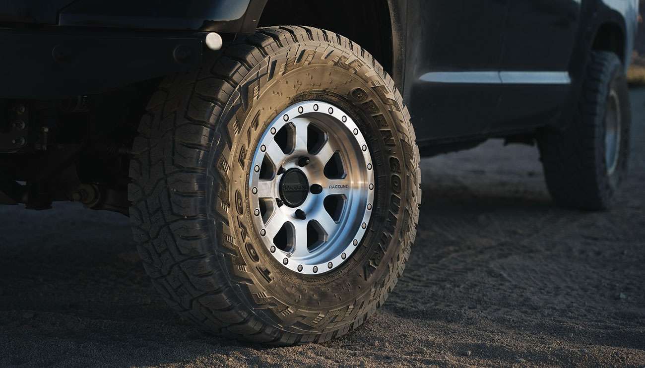 Close-up of a rugged Raceline wheel and tire on an off-road vehicle in a desert at sunset