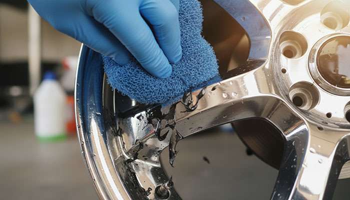 Gently removing softened paint from chrome wheel using nylon scrubber with proper technique