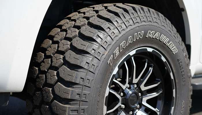 Close-up of a rugged off-road tire with deep treads mounted on a black alloy wheel on a white vehicle