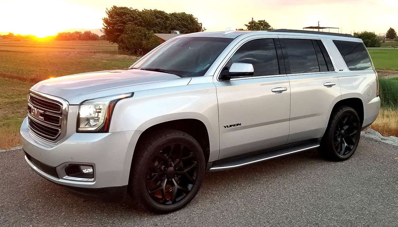 Close-up of a silver snowflake wheel on a black Yukon SUV in a bright setting