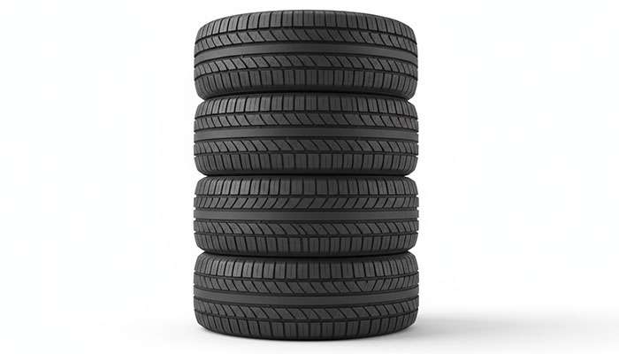 Stack of four new black car tires with detailed tread pattern on a white background