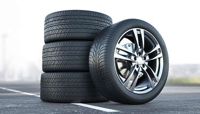 Stack of four black tires with one tire mounted on a silver alloy wheel on a road with blurred background