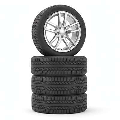 Stack of four black tires with one mounted on a silver alloy wheel on a blurred outdoor background