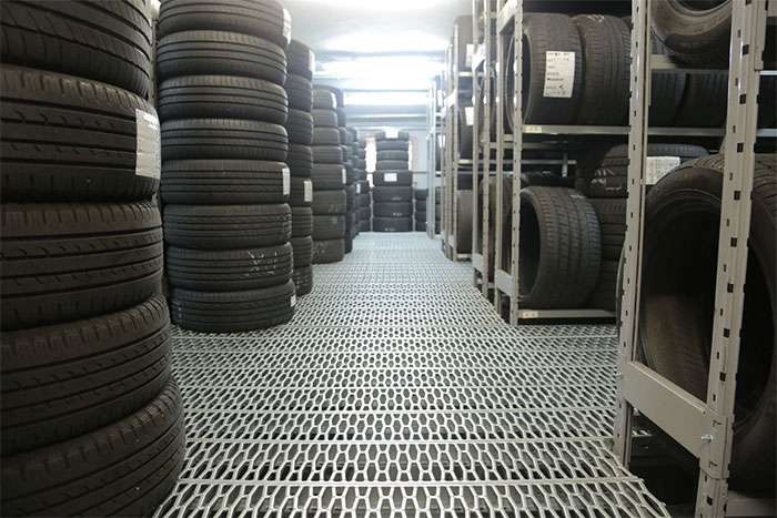 Rows of neatly stacked and shelved tires in a bright, organized storage facility with metal flooring.