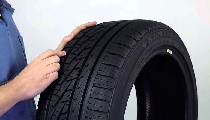 Person inspecting the tread pattern of a Sumitomo HTR A/S P02 tire against a plain background