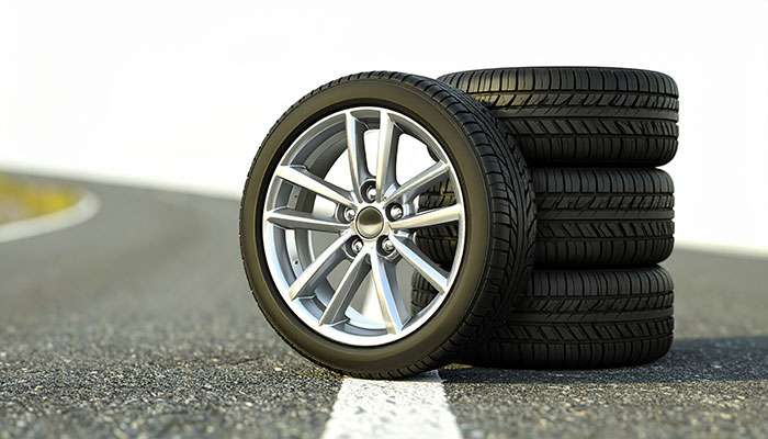 Stack of four car tires with one mounted on a silver alloy wheel on a road surface background