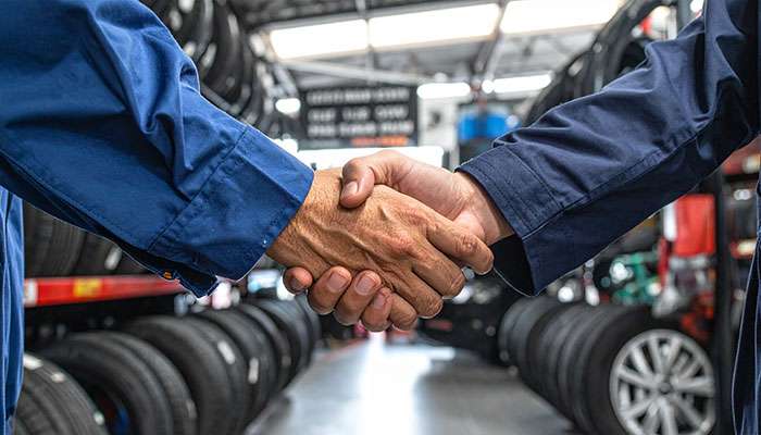 Two people shaking hands in a tire shop with a sign promoting lease-to-own financing up to $5,000.