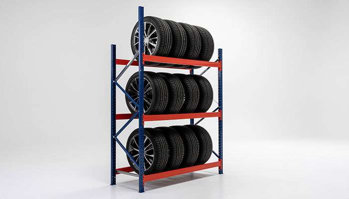 Adjustable red metal tire rack holding five car tires with silver rims on a white background