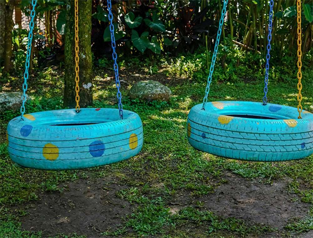 Two blue tires with colorful dots repurposed as swings hanging from chains in a green garden setting.