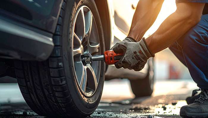 Mechanic wearing gloves using a power tool to tighten lug nuts on a car tire in a service garage.