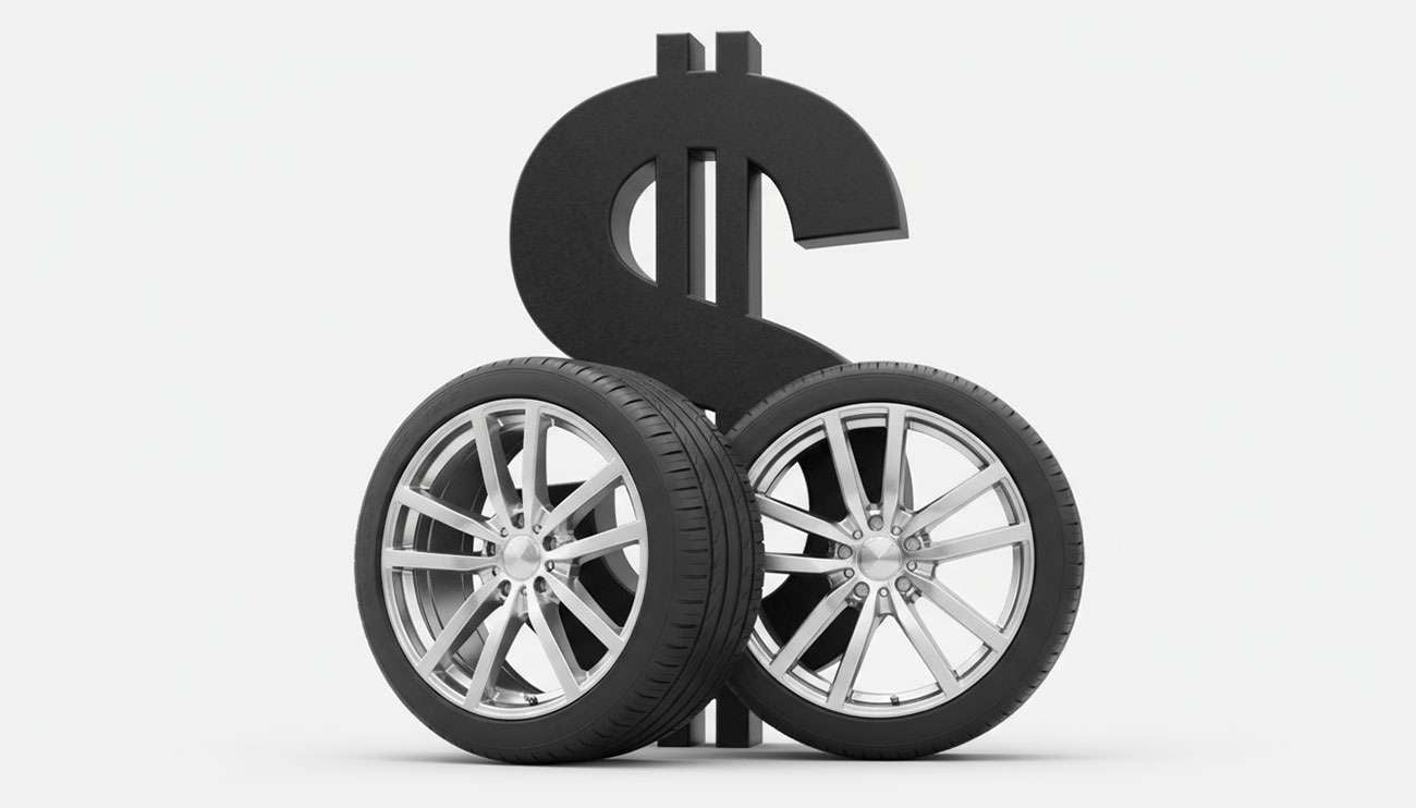 Two car tires with silver rims and a large black dollar sign behind them symbolizing tire cost concerns