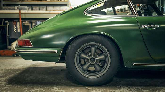 Close-up of a classic green car rear showcasing a vintage Torq Thrust mag wheel in a garage setting.