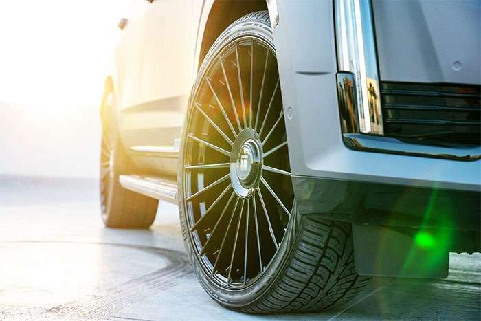 Close-up of a black Touren wheel with car tire on a silver vehicle in bright sunlight and lens flare
