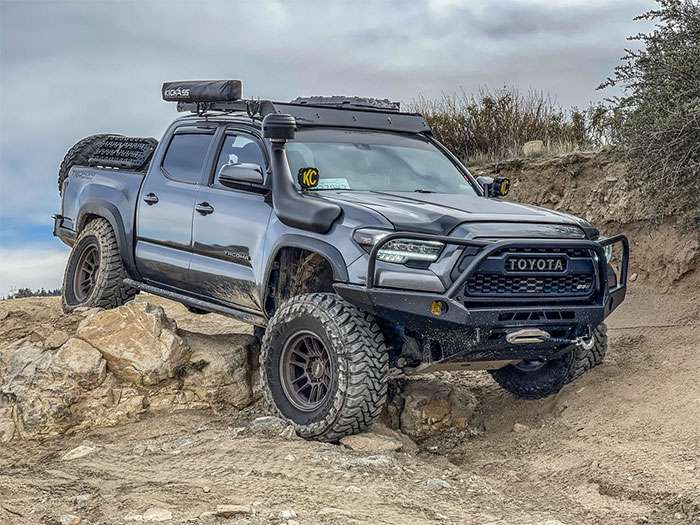 Toyota Tacoma TRD Off Road 4x4 climbing rocky terrain with off-road tires and roof-mounted gear under a cloudy sky