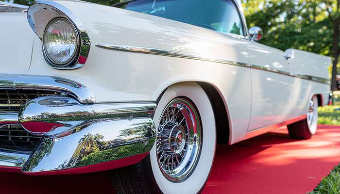 Vintage car with classic whitewall tires displayed on a red carpet at an outdoor event