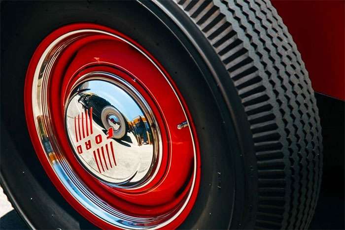 Close-up of a vintage Ford car tire with red rim and chrome hubcap reflecting the surroundings.