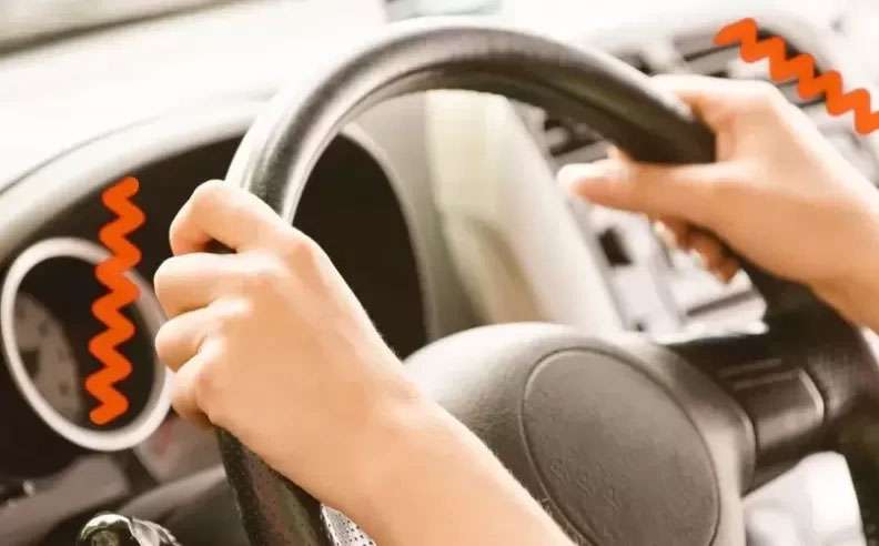 Hands gripping a car steering wheel with red vibration lines indicating steering wheel shaking or vibration issue.