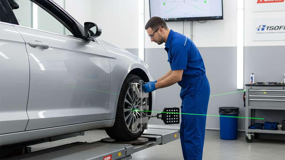Technician in blue uniform performing wheel alignment on a vehicle tire