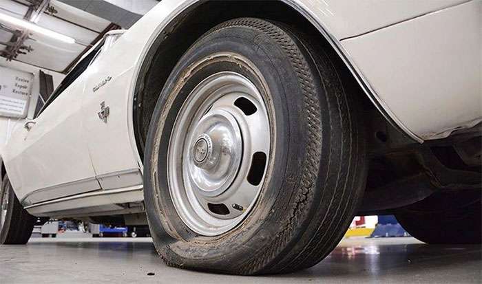 Close-up of a worn, flat tire on a white classic car inside a garage workshop