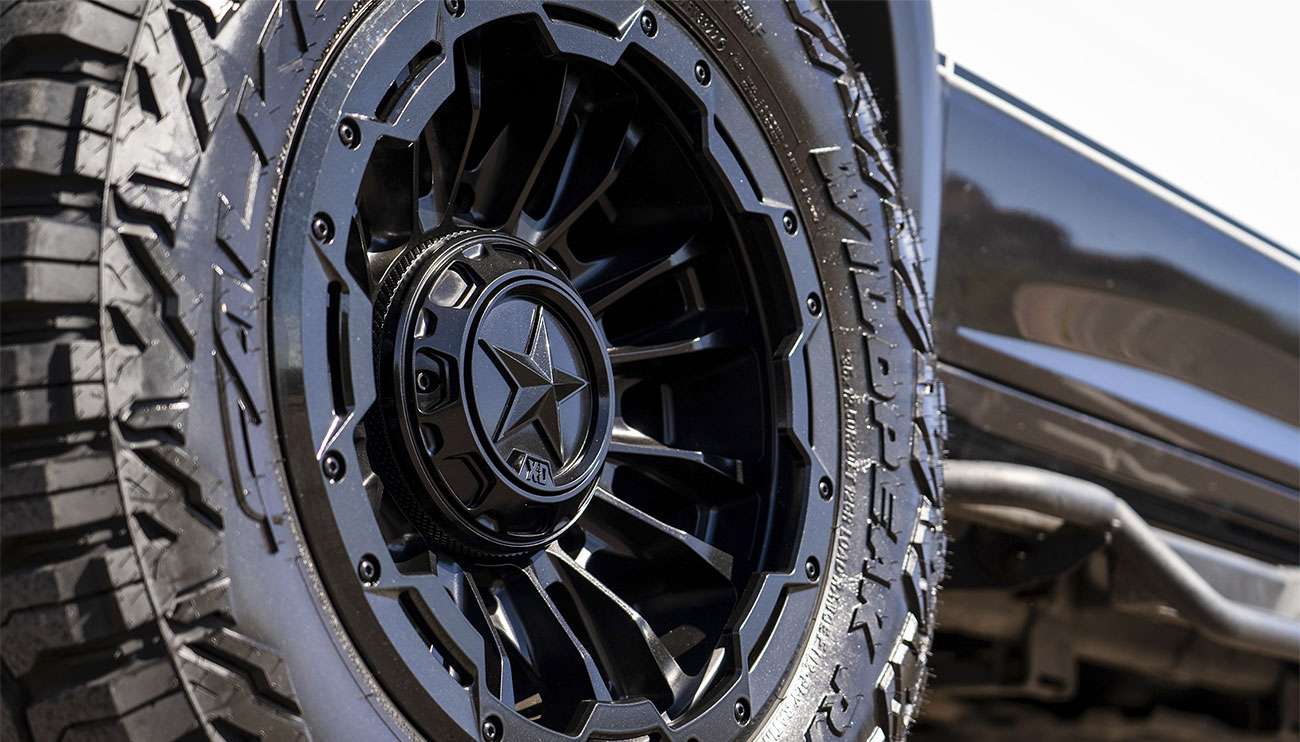 Off-road vehicle with XD series wheel kicking up dust at sunset in a desert setting