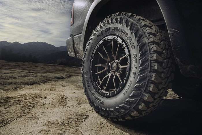 Close-up of a Yokohama Geolandar M/T G003 off-road tire mounted on a rugged vehicle in a mountainous terrain